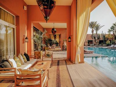 Covered terrace with comfortable seating next to a pool in a warmly designed hotel.