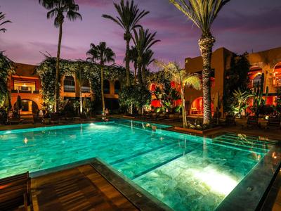 Illuminated pool at night surrounded by palm trees and a hotel building.
