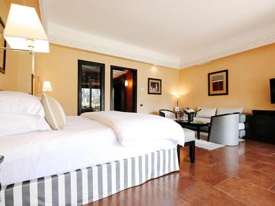 Bright hotel room with large bed, seating area, and TV on wooden floor.