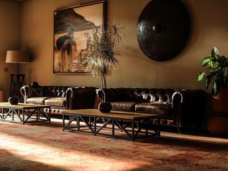 Gemütliches Wohnzimmer mit schwarzem Ledersofa, Holztischen, Pflanzen und warmem Licht.