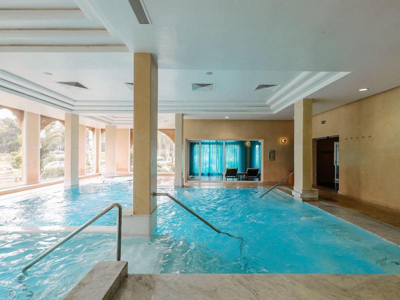 Hell beleuchteter Hallenpool mit Treppen, glattem Fliesenboden und großen Fenstern.