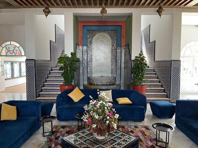 Wohnzimmer mit blauen Sofas, bunten Kissen, Blumenstrauß, symmetrischer Treppe und dekorativem Wandbrunnen.