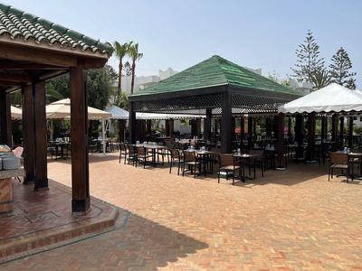 Restauracja na świeżym powietrzu z zielonymi i białymi markizami na brukowanym terenie z stołami i krzesłami.