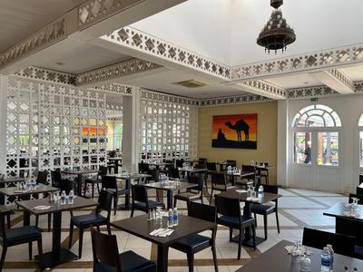 Nowoczesna restauracja z czarnymi stołami i krzesłami, jasne wnętrze i sztuka na ścianie.