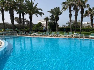 Duży basen hotelowy z leżakami i palmami w tle