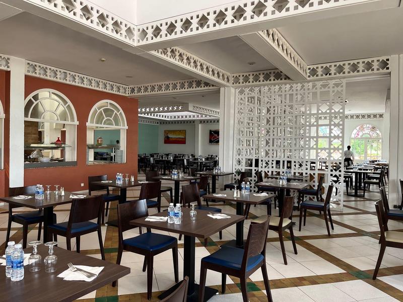 Jasna restauracja z dekoracyjnymi ścianami kratowymi, drewnianymi stołami i niebieskimi krzesłami.