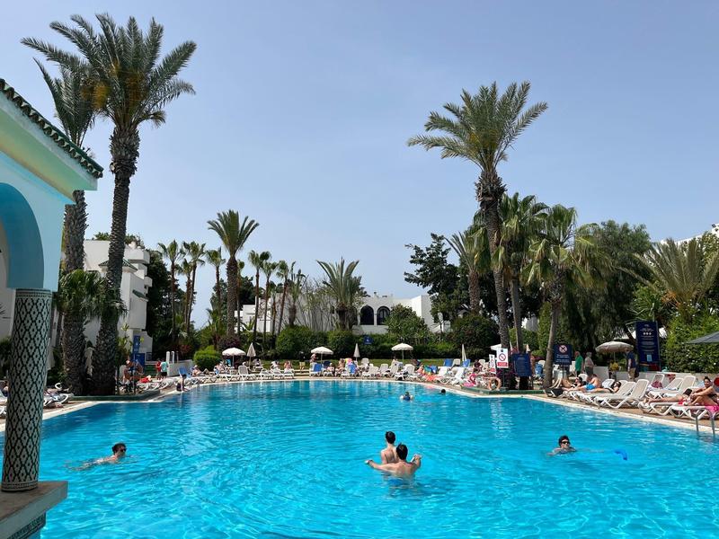 Duży basen hotelowy z palmami i leżakami pod czystym niebem.