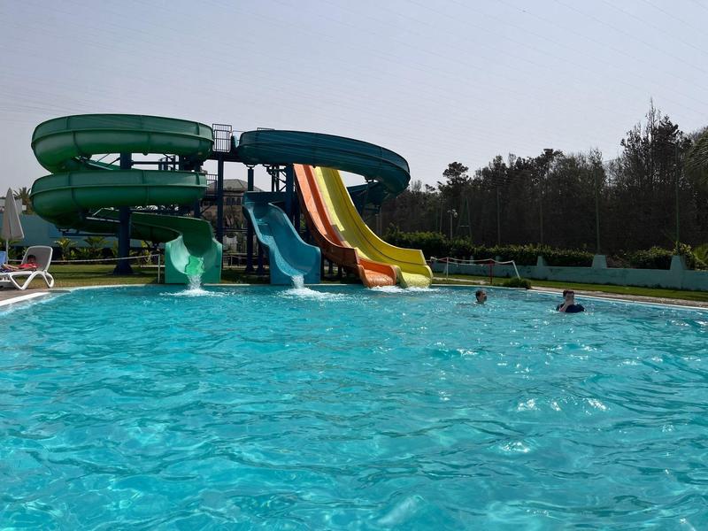 Park wodny z czterema zjeżdżalniami i gośćmi w dużym basenie pod czystym niebem.