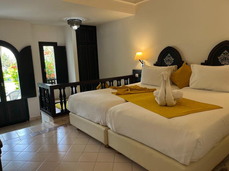 Jasny pokój hotelowy z dwoma łóżkami, żółtymi narzutami i dostępem do balkonu.