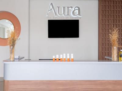 Moderner Empfangstresen mit weißen und hölzernen Akzenten, runder Spiegel, Trockenblumen und Bildschirm an der Wand.