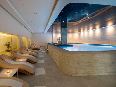 Moderner Innenpool mit LED-Beleuchtung, Liegestühlen und warmen Beige- und Blautönen.