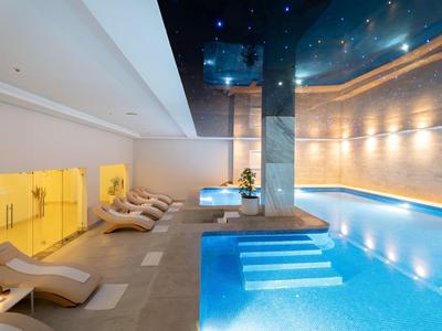 Moderner Indoor-Pool mit blau beleuchtetem Wasser, Liegestühlen und heller Wandbeleuchtung.