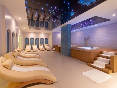 Área de spa moderna con tumbonas y jacuzzi bajo un techo iluminado con estrellas.