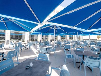 Gran terraza con sombrillas azules y mesas y sillas blancas a la luz del día.