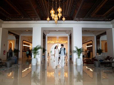 Ein elegantes Hotellobby mit glänzendem Marmorboden, weißen Säulen und zwei Personen in Anzug und Kleid.
