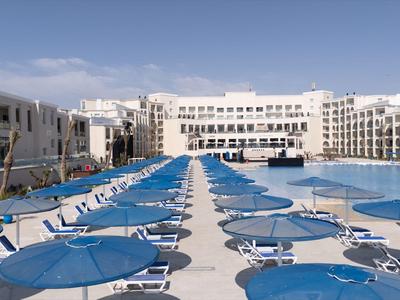 Gran área de piscina con sombrillas azules y tumbonas en un resort hotelero.
