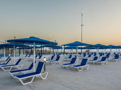 Leere blaue Liegestühle und Sonnenschirme stehen auf einer großen Terrasse bei Sonnenuntergang.