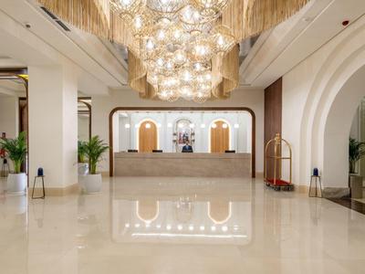 Große Hotellobby mit glänzendem Marmorboden, hellem Tresen und opulenter Deckenbeleuchtung.