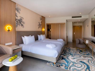 Hell eingerichtetes Hotelzimmer mit zwei Betten, modernem Teppich und Sitzbereich.