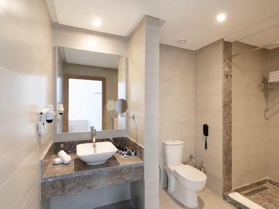 Modernes Badezimmer mit weißem WC, quadratischem Waschbecken, Spiegel und beiger Fliesenwand.