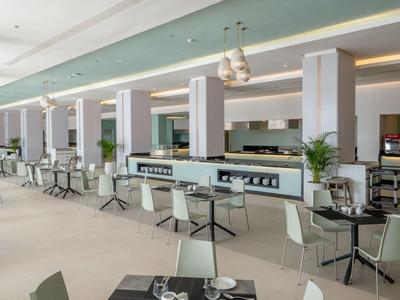 Área de comedor moderna y luminosa con sillas blancas, mesas y un mostrador central de servicio.