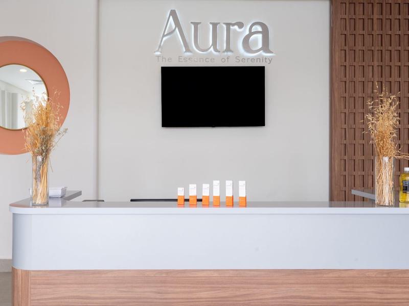 Moderner Empfangstresen mit weißen und hölzernen Akzenten, runder Spiegel, Trockenblumen und Bildschirm an der Wand.