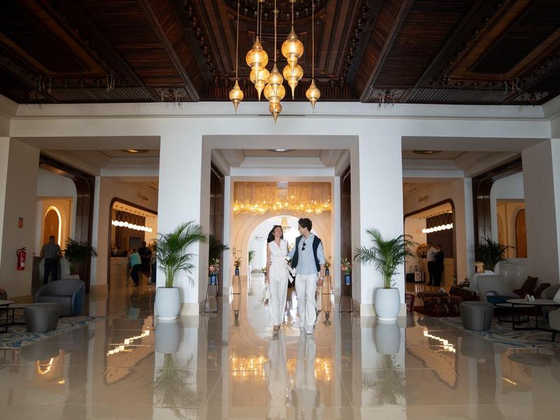 Ein elegantes Hotellobby mit glänzendem Marmorboden, weißen Säulen und zwei Personen in Anzug und Kleid.