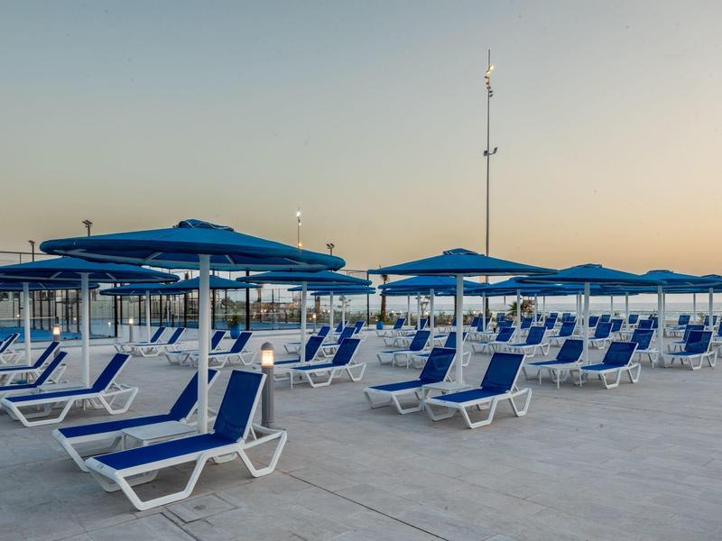 Leere blaue Liegestühle und Sonnenschirme stehen auf einer großen Terrasse bei Sonnenuntergang.