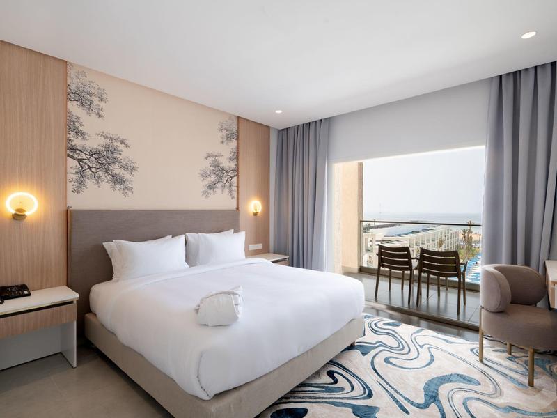 Modernes Schlafzimmer mit großem Bett, Balkon, hellen Wänden und Teppich mit blauem Muster.