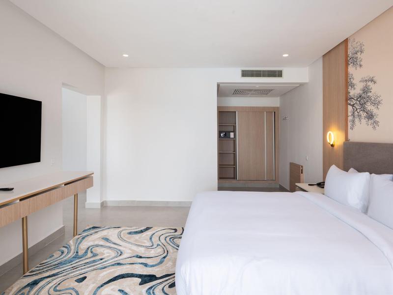 Modernes Hotelzimmer mit großem Bett, hellem Holzmöbel, Teppich und Wanddeko.