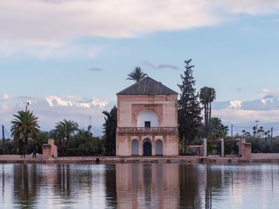 Kleines Gebäude am See mit Palmen und Bergen im Hintergrund bei Sonnenuntergang.