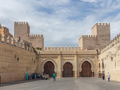 Alte Festungsmauern und Tore aus Sandstein mit Zinnen unter bewölktem Himmel.