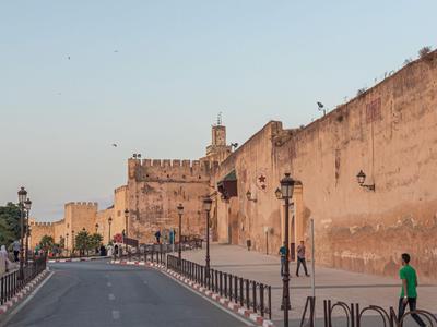 Breite Straße vor hohen, sandfarbenen Mauern einer historischen Festung bei Sonnenuntergang.