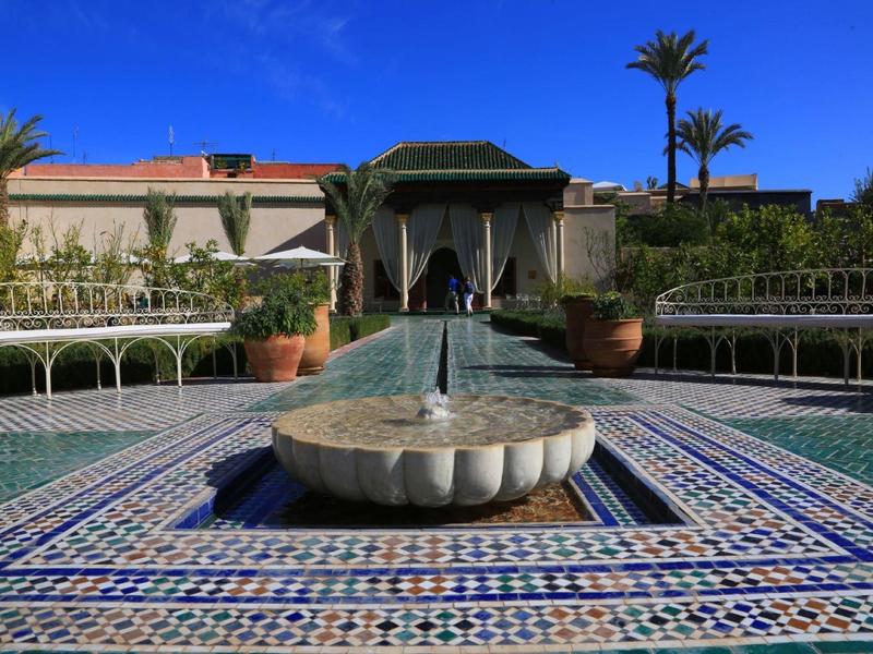 Ein Garten mit blau-weiß gemustertem Mosaik, Springbrunnen, grünen Pflanzen und einem Pavillon.