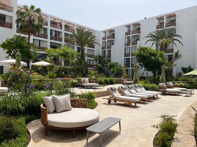 Moderner Hotelgarten mit runden und rechteckigen Liegestühlen, umgeben von Palmen und Blumen.