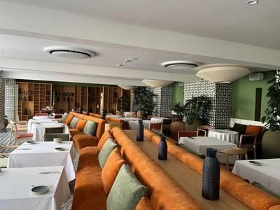Modern dining room with white tables, orange sofas, and wood decor.