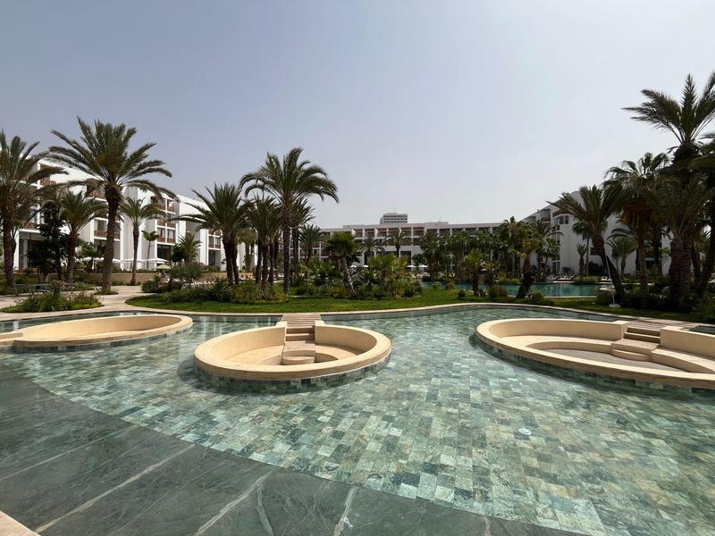 Pool mit kreisförmigen Sitzbereichen und Palmen im Hintergrund in einer Hotelanlage.