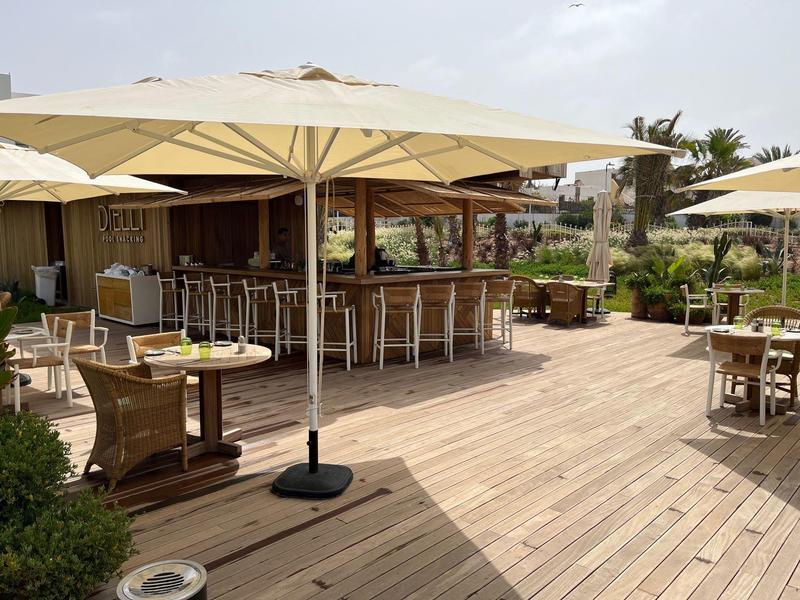 Große Terrasse mit Holzfußboden, Tischen, Stühlen und Sonnenschirmen neben einer Bar.