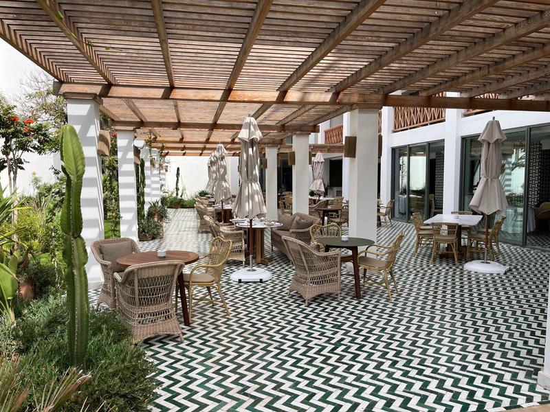 Überdachte Terrasse mit Mustervorlege aus Fliesen und mehreren Tischen und Stühlen in einem Hotel.