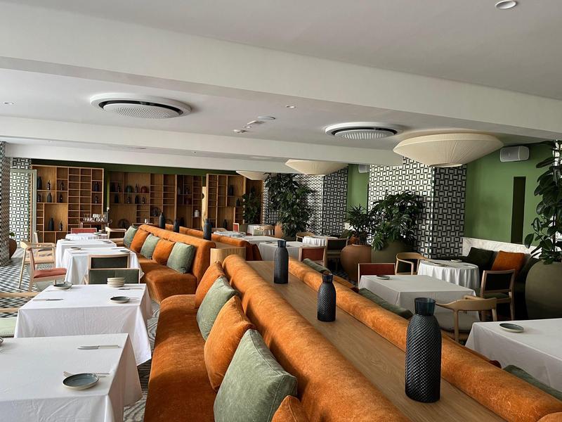 Modernes Restaurant mit weißen Tischdecken, orangen Sitzbänken und stilvoller Dekoration.