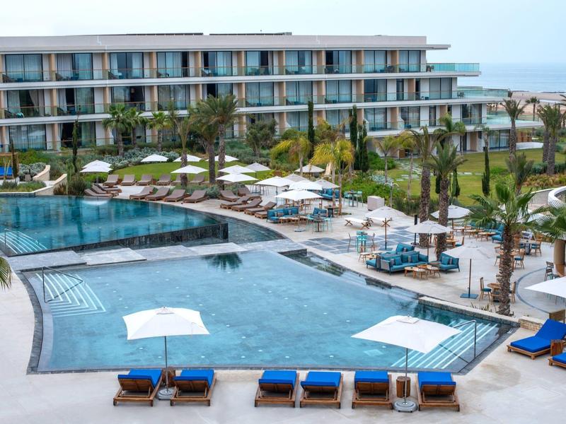 Modern hotelzwembad met ligstoelen en palmbomen, omgeven door een meerlaagse structuur.
