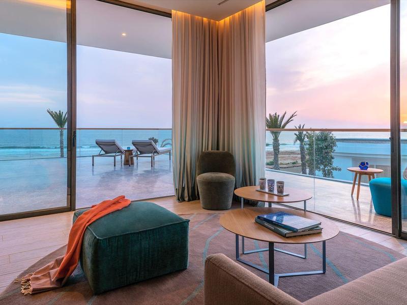 Moderne woonkamer met panoramisch zeezicht en terras bij zonsondergang.