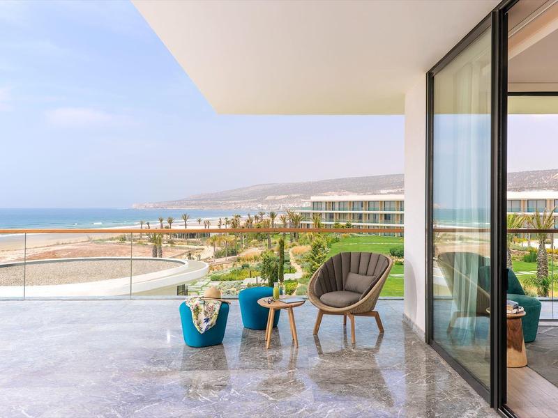 Modern balkon met stoel en zeezicht, grenzend aan een slaapkamer met glazen wanden.