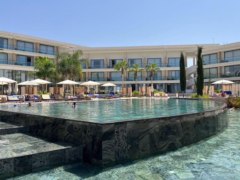 Modern hotelzwembad met ligstoelen en parasols onder een blauwe lucht.