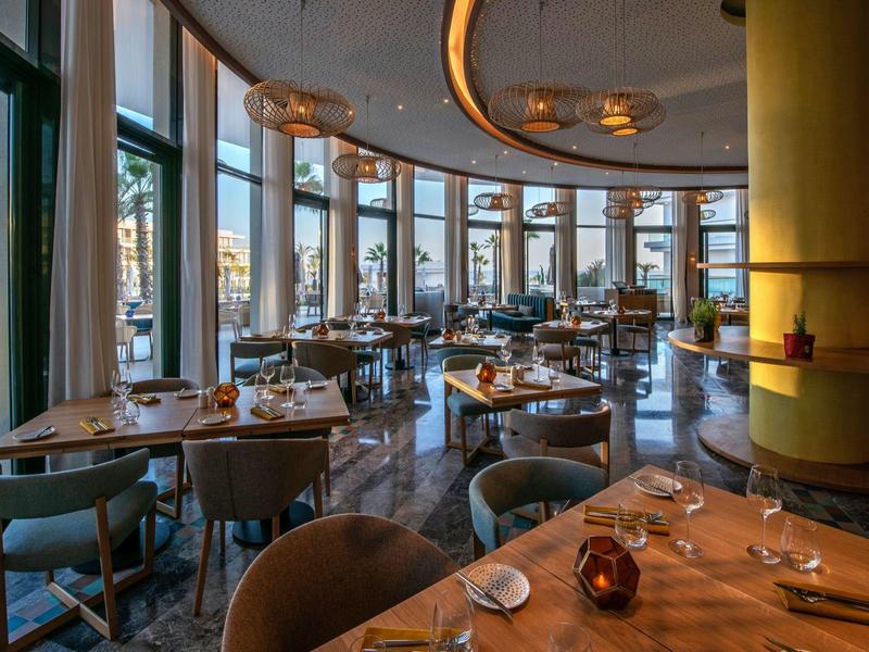 Elegant restaurant met moderne meubels en grote ramen met uitzicht naar buiten.