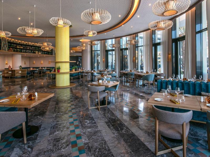 Modern hotelrestaurant met grote ramen, stijlvolle stoelen en elegante verlichting.