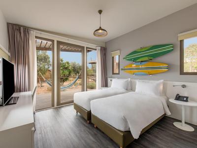 Chambre d'hôtel moderne avec lit double, planches de surf au mur et vue sur une terrasse.