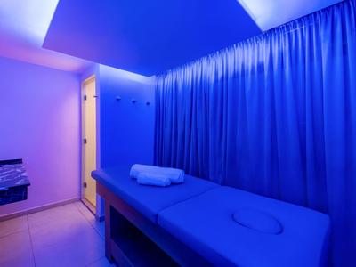 Treatment room with massage table and towels, blue lighting, curtain in the background.