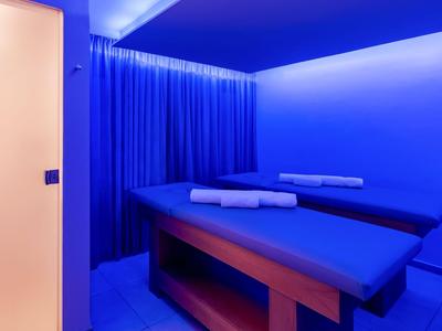 A calm wellness room lit with blue lights featuring two massage tables and blue curtains.