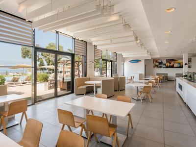 Bright dining area with tables, chairs, large windows, and a view of an outdoor area.
